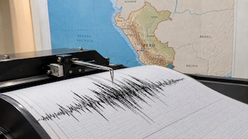 Primer plano de un sismógrafo registrando ondas sísmicas en un papel cuadriculado, con un mapa de Perú, Ecuador, Brasil y Bolivia al fondo