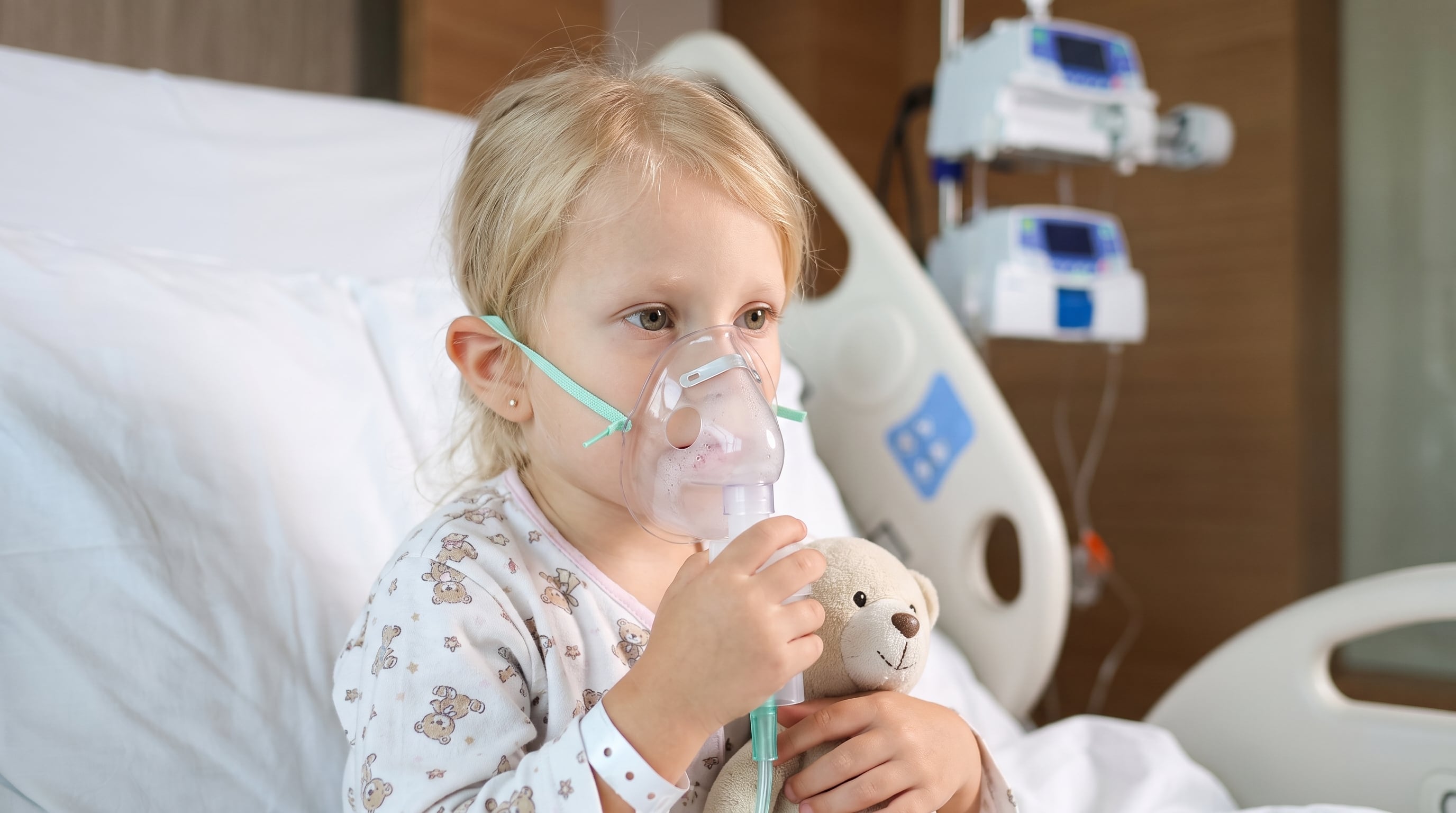 Una niña con fibrosis quística recibe tratamiento nebulizador en una cama de hospital mientras sostiene un oso de peluche. (Imagen Ilustrativa Infobae)