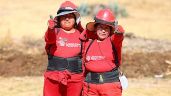 Dos mujeres con casco e indumentaria de color rojo con el logotipo de Llamkasun Perú levantan los pulgares al aire libre