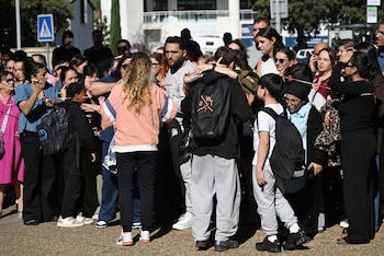 Un grupo de personas y jóvenes con mochilas se congrega detrás de una cinta de seguridad en la vía pública