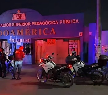 Vista nocturna de la fachada principal de la EESP Indoamérica en Trujillo, con su letrero iluminado y varios agentes policiales junto a motocicletas frente a la entrada