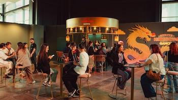 Personas sentadas en banquetas junto a mesas altas frente a una barra circular iluminada y un panel con la figura de un dragón