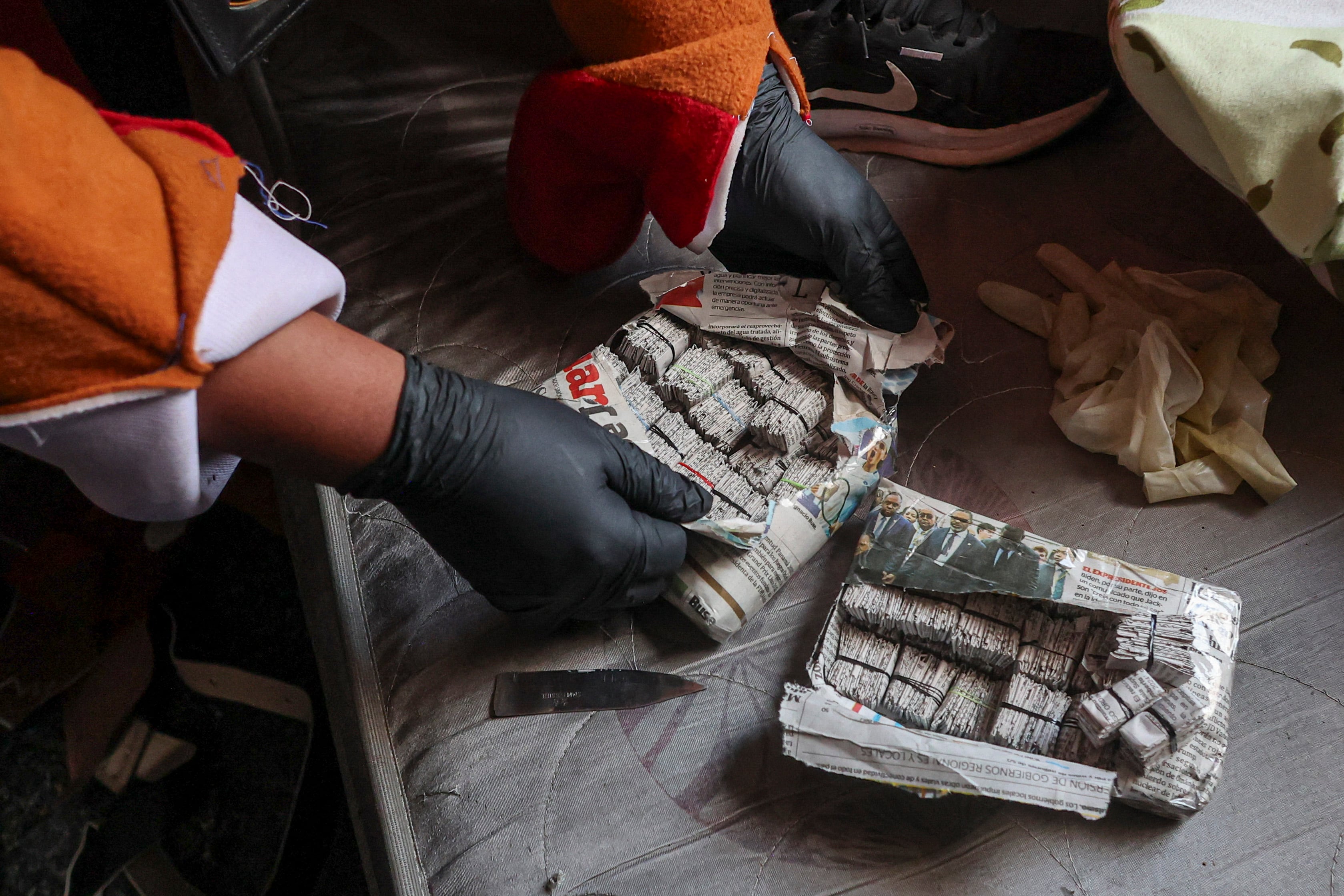 Un agente de la Policía de Perú, vestido con un disfraz de mascota del Mundial 2026, inspecciona paquetes de droga incautados durante un operativo contra el narcotráfico en San Juan de Lurigancho. (AFP)