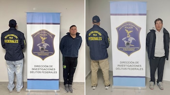 Dos hombres detenidos permanecen de pie junto a efectivos policiales de espalda y carteles con el escudo de la policía de Buenos Aires.