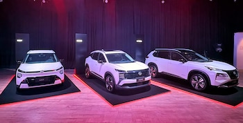 Tres automóviles SUV de color blanco sobre plataformas con iluminación roja inferior frente a un telón de fondo oscuro