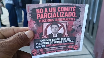 Primer plano de una mano sosteniendo un cartel de protesta rojo y negro en español, exigiendo elecciones transparentes y la renuncia de Julio Edgar López Cervantes