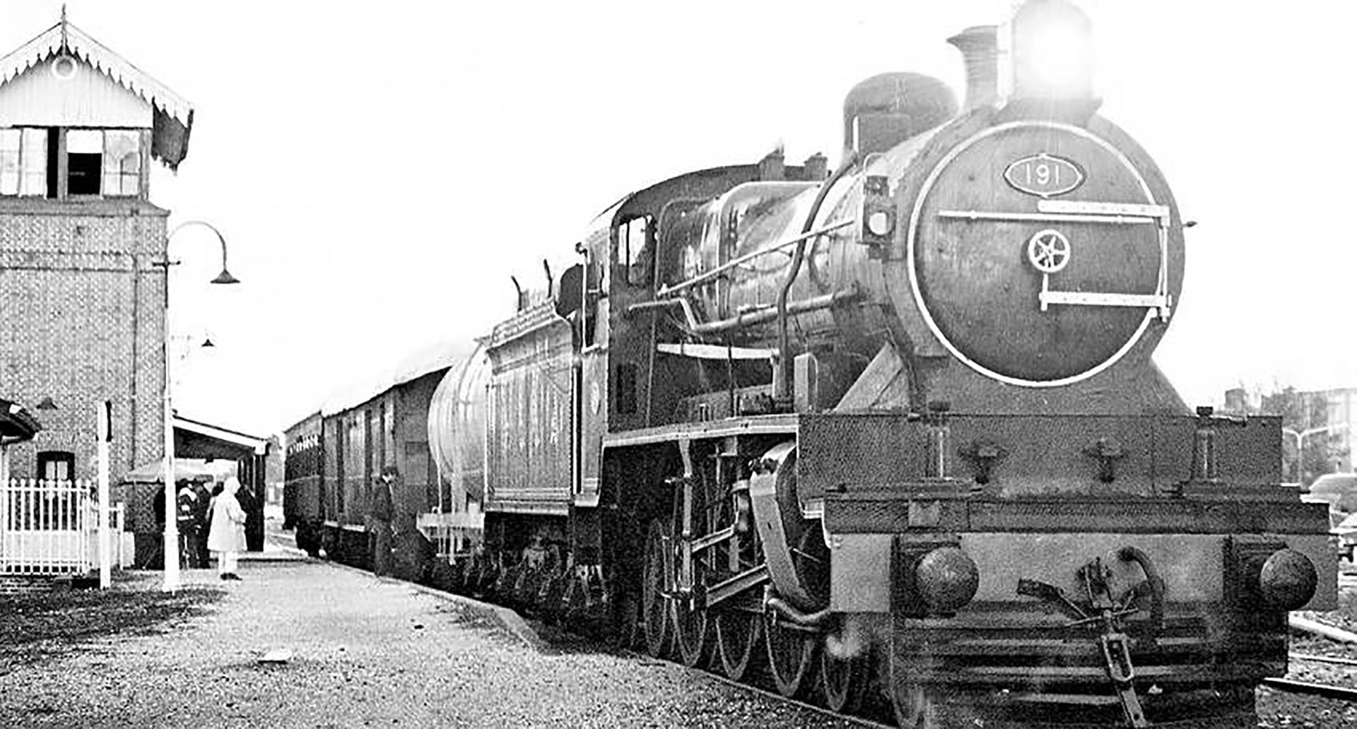 Una locomotora de vapor del Ferrocarril Central Norte se detiene en una estación, con pasajeros y personal esperando en el andén.