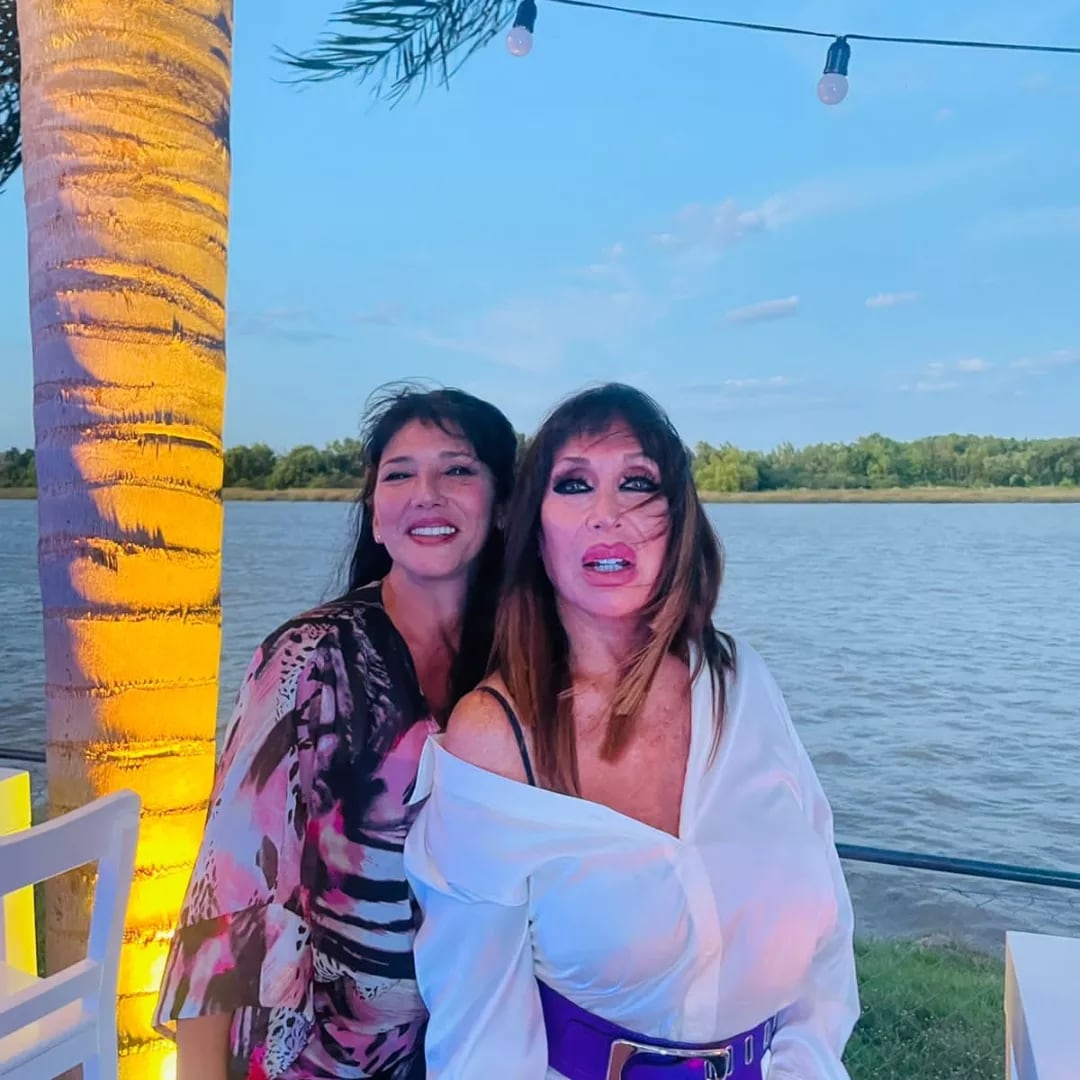 Moria Casán posa junto a su amiga Zeta a orillas del agua en un espacio al aire libre.