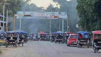 Numerosos mototaxis, personas y humo en una calle. Un cartel azul con la palabra "Nauta" y un semáforo rojo se ven en el fondo
