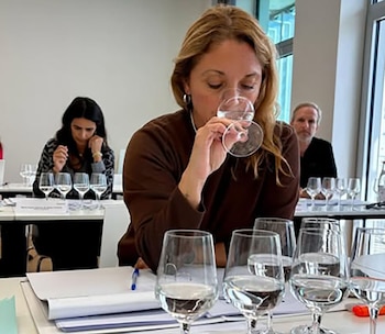 Analía Videla, sommelier de agua, en primer plano oliendo un vaso de agua. Al fondo, más participantes y copas de agua en una sala de cata