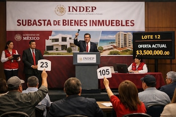Un hombre con martillo en podio de subasta INDEP con cartel de "Subasta de Bienes Inmuebles". Asistentes con paletas y pantalla digital con "Oferta Actual $3,500,000.00".