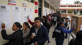 Personas en una larga cola consultan carteles con DNI en mano en un centro de votación exterior en Perú; personal de ONPE asiste a votantes.