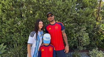 Un hombre, una mujer y un niño posan frente a vegetación. La mujer viste camiseta de Argentina; el hombre y el niño visten camisetas de España.
