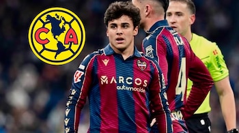 Un futbolista con uniforme azul y grana en el campo junto al escudo del Club América en la esquina izquierda y un árbitro al fondo.