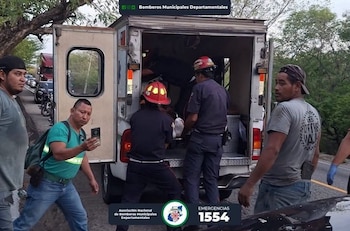 Integrantes de cuerpos de socorro con casco mueven a un paciente en la parte trasera de una ambulancia junto a la carretera