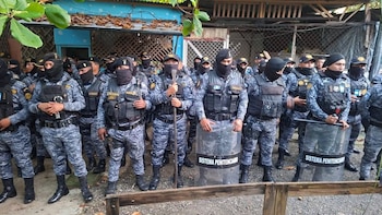 Grupo de agentes uniformados con camuflaje, chalecos tácticos, pasamontañas negros, gorras, algunos con bastones y escudos que leen 'Sistema Penitenciario'
