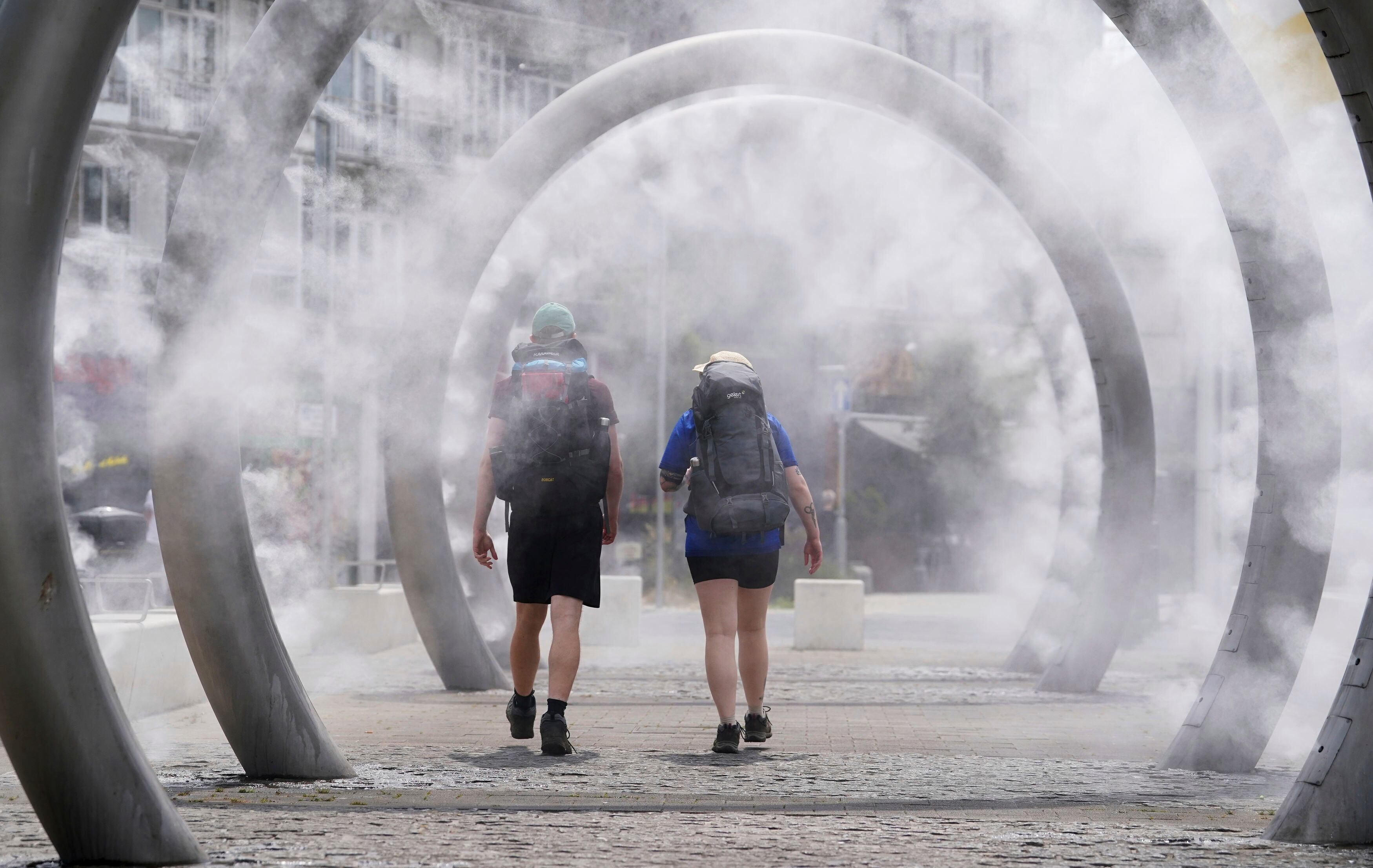 Caminantes pasan por debajo de unos arcos que pulverizan agua en forma de niebla fina, en Dover, Inglaterra