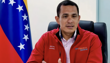 Hombre sentado, viste chaqueta roja con insignias "Mstro Allcrias" y "DPP Comercio Nacional" sobre camisa. A su izquierda, bandera de Venezuela