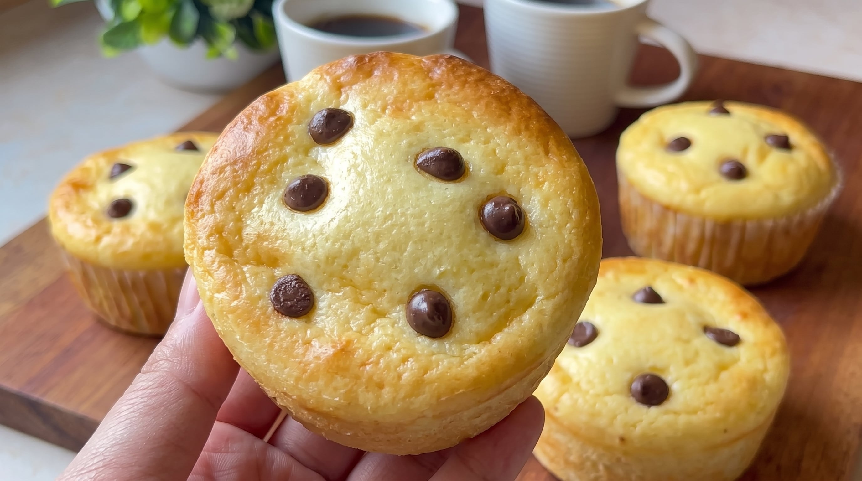 Una persona sostiene un pan de leche con pepitas de chocolate junto a otros bollos e infusiones sobre una tabla de madera. (Imagen Ilustrativa Infobae)