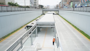 Vista elevada de una estación y carril exclusivo de autobuses en una vía desnivelada, con un autobús blanco a la izquierda y un trabajador con casco