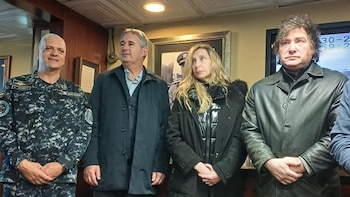 Cuatro personas, incluyendo a Javier Milei en chaqueta de cuero, posan de pie en un interior con un militar argentino, un hombre de saco y una mujer de chaqueta oscura