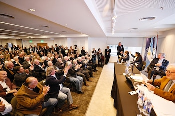 Un grupo numeroso de personas en un auditorio aplaude frente a una mesa directiva con banderas