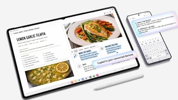 Una tableta digital con una receta de cocina abierta en pantalla, un lápiz óptico blanco y un teléfono inteligente que recibe texto copiado