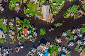 Vista cenital de casas sobre pilotes, parcelas de vegetación y canoas que navegan por canales de agua oscura