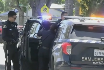 Tres agentes de policía uniformados permanecen junto a una patrulla de la ciudad de San José con luces de emergencia encendidas