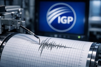 Sismógrafo profesional con una aguja dibujando ondas sísmicas en papel cuadriculado. Al fondo, una pantalla muestra el logo del Instituto Geofísico del Perú, IGP.