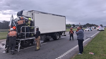 Un camión blanco accidentado en el arcén de una carretera con varios bomberos subidos a una plataforma asistiendo en la cabina