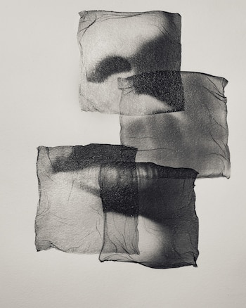 Composición en blanco y negro con tres formas cuadradas oscuras y translúcidas superpuestas, que muestran una textura fina y arrugada sobre un fondo claro
