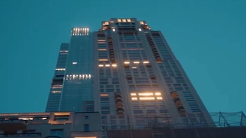 Vista en contrapicada de un rascacielos alto con fachada de ventanas y balcones, algunas iluminadas, contra un cielo azul oscuro