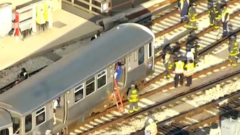 Vista aérea de un tren gris estacionado en las vías, con personal de emergencia en uniformes ayudando a evacuar pasajeros usando una escalera