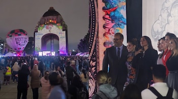 Un globo aerostático iluminado ante el Monumento a la Revolución con una multitud y un grupo de personas posando en un escenario.