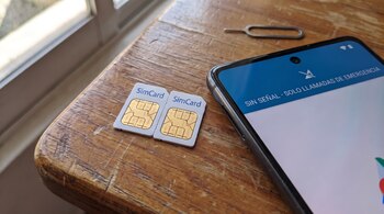 Dos tarjetas SimCard, un teléfono móvil con pantalla que indica "sin señal", y una herramienta de extracción de SIM, sobre una superficie de madera.