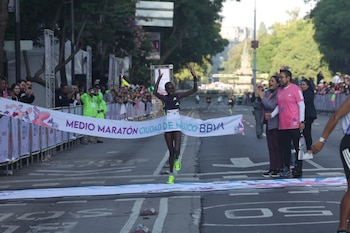 Corredora cruza línea de meta con brazos levantados. Banner blanco dice 'MEDIO MARATÓN CIUDAD DE MEXICO BBVA'. Público observa detrás de vallas