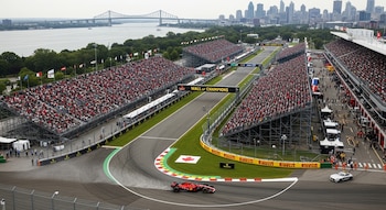 Vista aérea del Circuito Gilles-Villeneuve durante el GP de Canadá. Un coche rojo de F1 en pista, gradas repletas de aficionados, y el horizonte de Montreal con un puente.