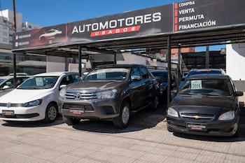 Letrero de Automotores Usados, tres automóviles exhibidos: un Volkswagen blanco, una Toyota Hilux gris y un Chevrolet negro. Etiquetas de año 2020 y 2016