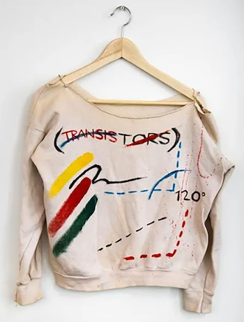 Sudadera clara con la palabra '(TRANSISTORS)' tachada en rojo y azul, trazos gruesos en amarillo, rojo y verde, líneas punteadas, salpicaduras y '120°', colgada en un gancho de madera