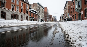 Vista de una calle de ciudad despejada y húmeda en invierno, con montículos de nieve a los lados y edificios de ladrillo a lo largo de la vía.
