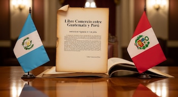 Banderas de Guatemala y Perú flanquean un documento con el título 'Libre Comercio entre Guatemala y Perú' y la fecha de entrada en vigor, sobre una mesa de madera.