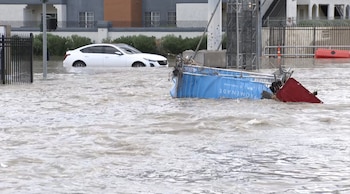 Un automóvil blanco y un carro de compras tumbado en una calle inundada por agua corriente