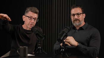 Dr. Marc Brackett, con gafas y camisa negra, gesticula a la izquierda de un micrófono, mientras otro hombre barbudo con camisa negra está a la derecha
