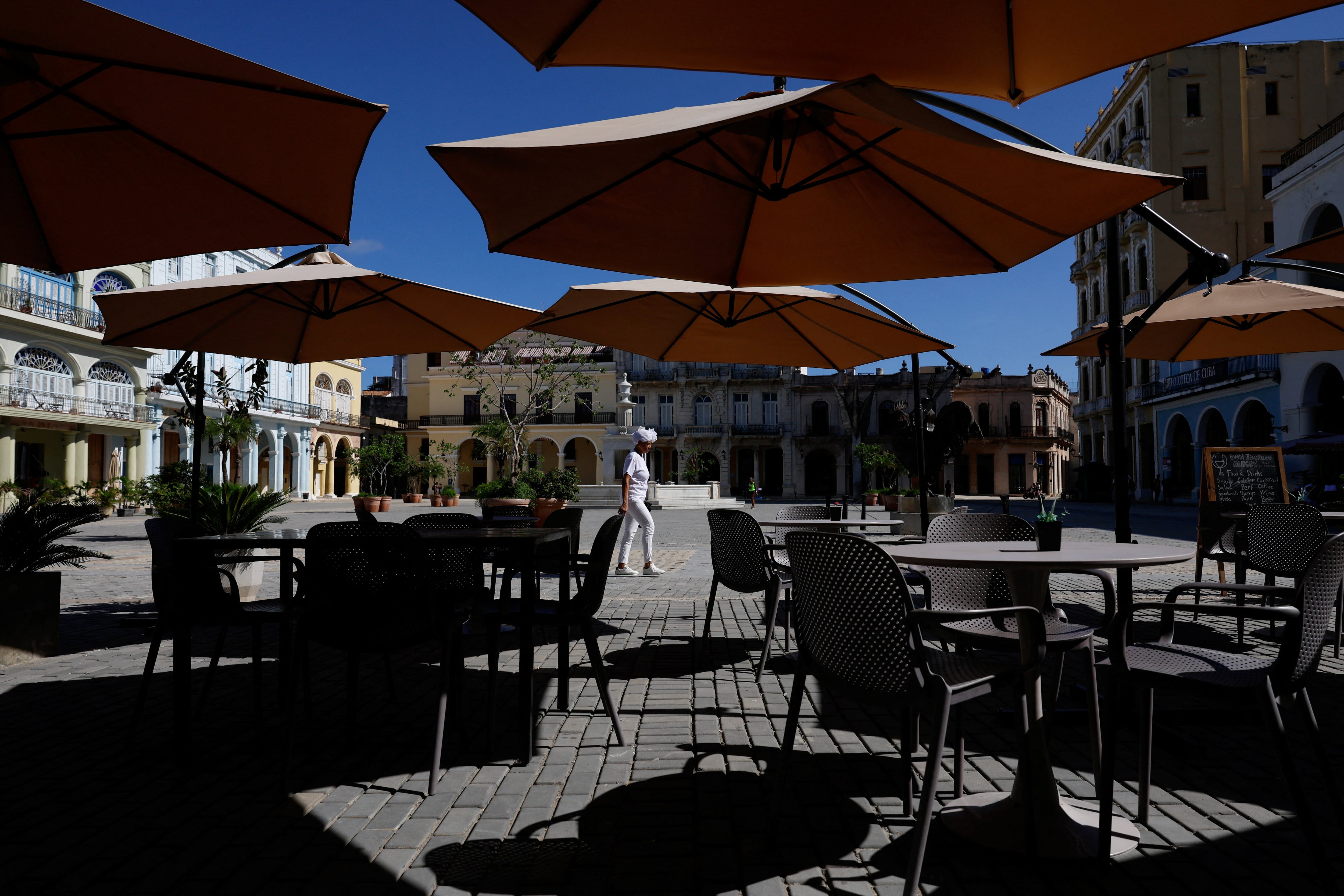 Una santera, sacerdotisa de la religión afrocubana Santería, pasa junto a un café vacío en la Plaza Vieja, uno de los lugares turísticos más populares de La Habana Vieja, ya que las sanciones estadounidenses han provocado que la mayoría de las principales empresas de turismo y viajes abandonen la isla o reduzcan drásticamente sus operaciones, en La Habana, Cuba, el 8 de junio de 2026. REUTERS/Norlys Pérez