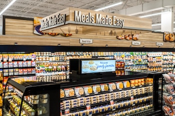 Mostradores refrigerados con envases de comida preparada bajo letreros con el texto Meals Made Easy en un supermercado