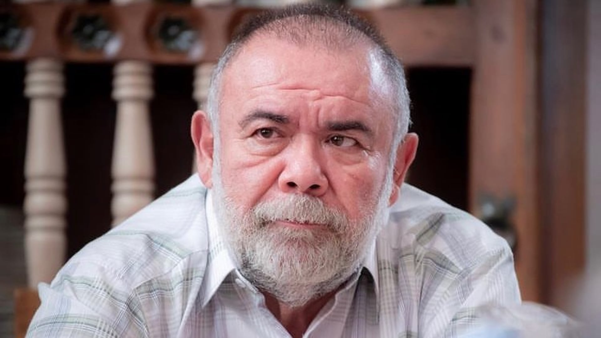 El actor Jesús Ochoa viste una camisa a cuadros claros frente a una estructura de madera en un espacio interior. (Instagram: Jesús Ochoa)