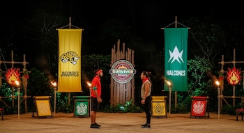 Un hombre y una mujer se enfrentan en una arena nocturna con antorchas. Banderas de Jaguares y Halcones y el logo de Survivor México son visibles.