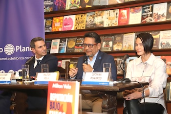 Tres personas, Milton Vela al centro, Sebastián Arcuri a la izquierda y Luciana Olivares a la derecha, sentadas en una mesa frente a una estantería de libros