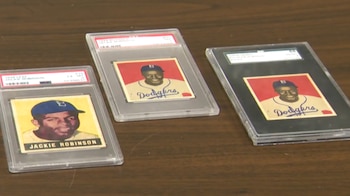 Tres tarjetas de béisbol de Jackie Robinson encapsuladas en estuches protectores transparentes se muestran sobre una mesa de madera oscura
